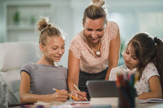 A beautiful single mother helping hers two daughters with homework at home.