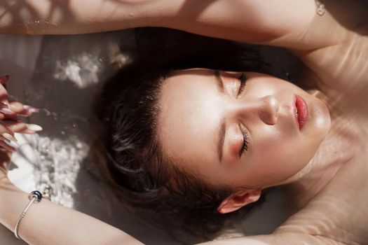 An Attractive girl relaxing in bath with closed eyes on light background