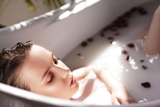 An Attractive girl relaxing in bath with petals on light background