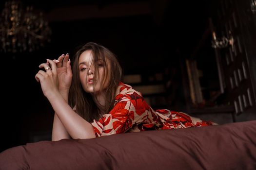 Relaxed woman lying on a brown bed thinking deeply. Woman in retro style room in red dress - fashion style