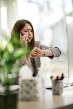 A young business woman looking stressed out while talking on smartphone in her home office.