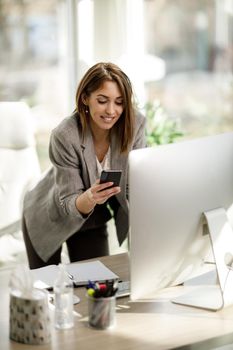 An attractive business woman using smartphone while working at computer in her office.