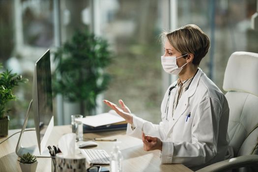 A female doctor with protective face mask working online in her consulting room during COVID-19 pandemic.
