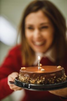 Cropped shot of a smiling woman holding a birthday cake with candles and having online party with friends.