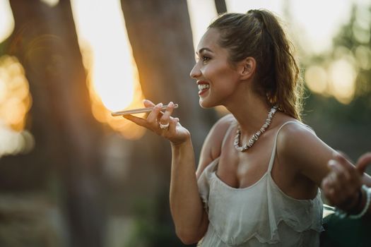 Young happy woman talking voice message on a smartphone while enjoying summer vacation.