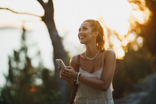Young attractive smiling woman using a smartphone while enjoying walk in the park at summer vacation.