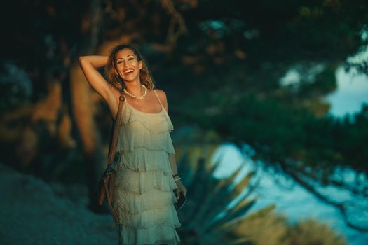 A smiling young woman enjoying a summer vacation while walking through pine forest near Mediterranean sea.