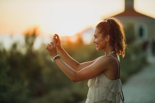 A young smiling woman taking photos with her smartphone while enjoying a summer vacation.