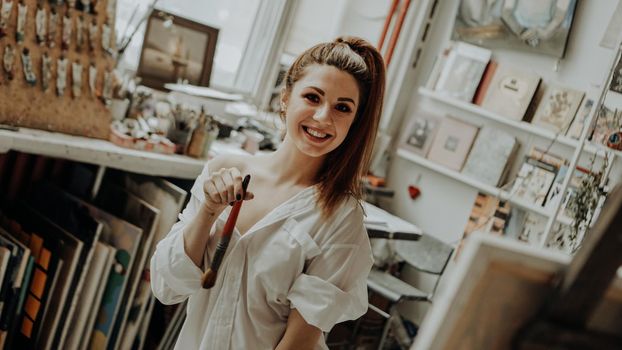 Portrait of happy smiling female artist with brush in art workshop. Selective focus. Vintage style photo