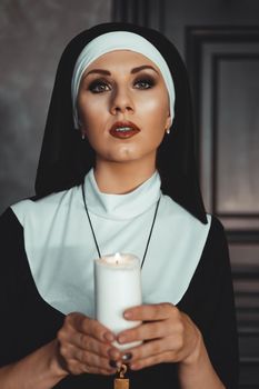 Young catholic nun is holding candle in her hands. Photo on black background. Portrait of beautiful woman