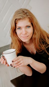 Woman holds a cup of coffee in the morning in Christmas kitchen. Happy young woman having fun and smiling