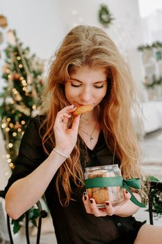 Happy young woman having eating christmas cookies in kitchen and smiling