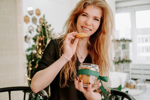 Happy young woman having eating christmas cookies in kitchen and smiling