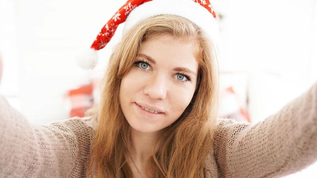 Christmas portrait of beautiful girl. Teenager wearing santa claus hat. Girl smiling and making selfie