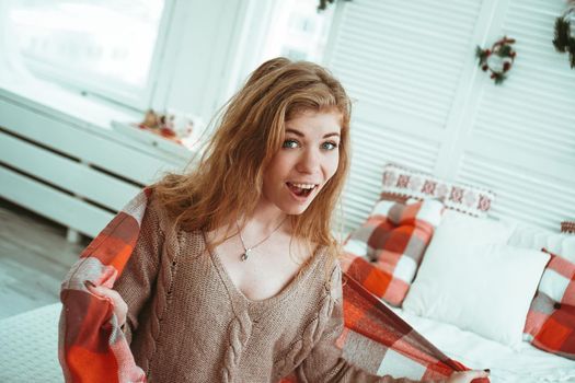 A beautiful laughing young Russian woman in a red plaid at home