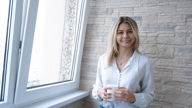 Business woman with white cup of coffee looking out the window - brick wall background