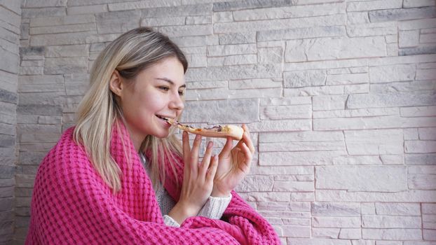 Beautiful woman with pink plaid holds a slice of pizza in her hand and eats it. Close-up
