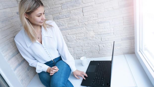 Side view. Young business woman with a cup of coffee sitting and taking notes in notebook. Student learning online. Blogger with laptop.