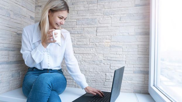 Side view. Young business woman with a cup of coffee sitting and taking notes in notebook. Student learning online. Blogger with laptop.