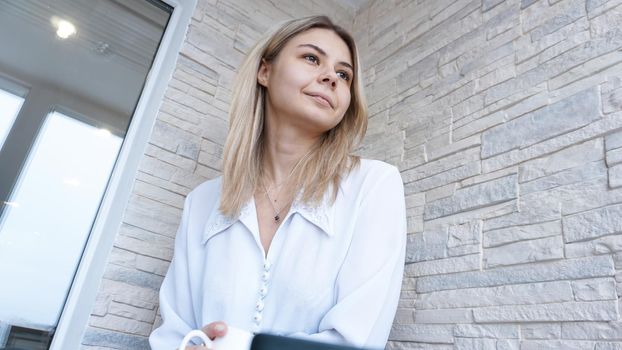 Side view. Young business woman with a cup of coffee sitting and taking notes in notebook. Student learning online. Blogger with laptop.