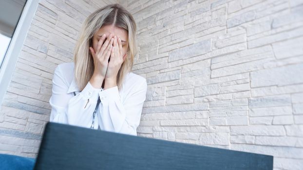 Woman looks at her laptop with a pained worried expression. Female employee is stressed out of work, touching aching head, reading email, solving a problem.