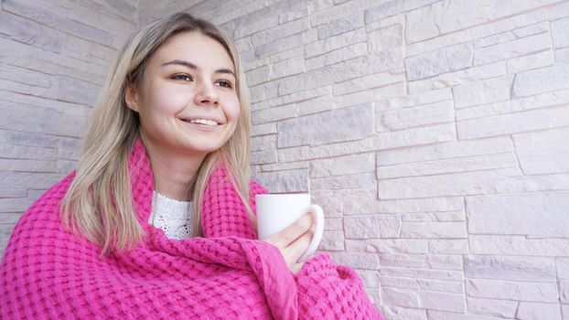 Beautiful young girl in a pink plaid with a cup of coffee. Young woman on balcony. Rest for a cup of coffee for cozy breakfast.