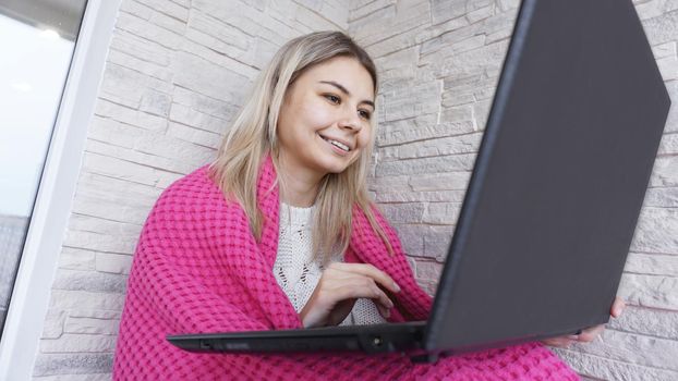 Beautiful smiling young woman with a laptop and warm plaid on a white brick background