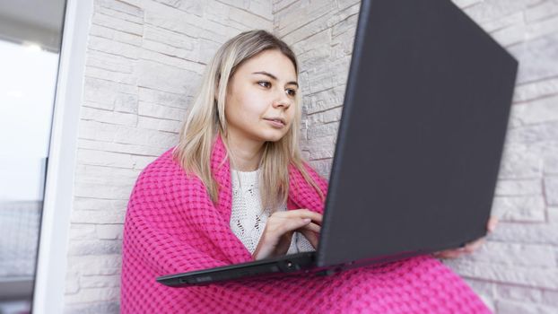 Beautiful smiling young woman with a laptop and warm plaid on a white brick background