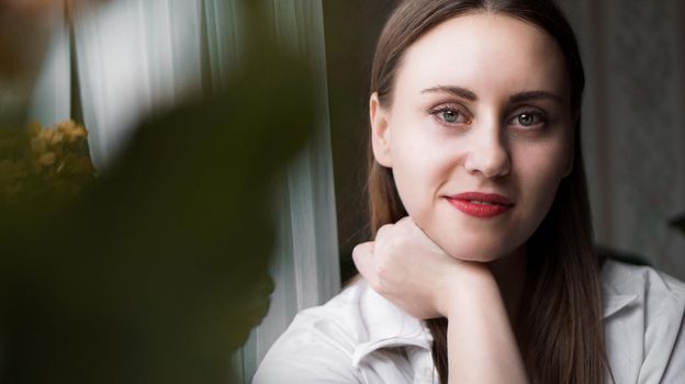 Portrait of attractive brunette woman. Home portrait of a woman with red lips in a white shirt