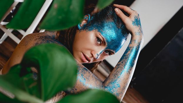 Portrait of a beautiful woman posing like in the wild forest. Woman with blue sparkles on her face. People are different from others. Individuality