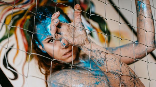 Brunette girl behind the net. Portrait of beautiful woman with blue sparkles on her face. The concept of people with Individuality