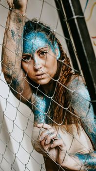 Brunette girl behind the net. Portrait of beautiful woman with blue sparkles on her face. The concept of people with Individuality
