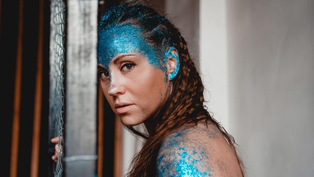 Portrait of beautiful woman with blue sparkles on her face. The concept of freaks and aliens. People are different from others. Individuality
