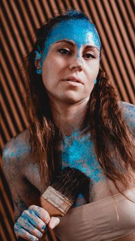 Portrait of beautiful girl with blue facial bodyart with sequins. The artist draws body art on herself