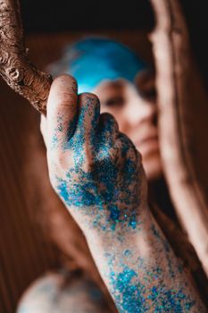 Portrait of a beautiful woman posing like in the wild forest. Woman with blue sparkles on her face. People are different from others. Individuality