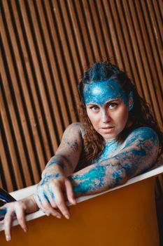 Portrait of beautiful woman with blue sparkles on her face in the bath. The concept of Individuality