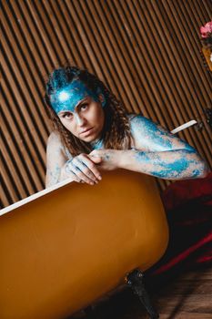 Portrait of beautiful woman with blue sparkles on her face in the bath. The concept of Individuality