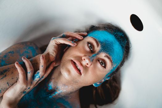 Portrait of beautiful woman with blue sparkles on her face in the bath. The concept of Individuality