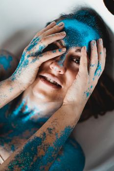 Portrait of beautiful woman with blue sparkles on her face in the bath. The concept of Individuality