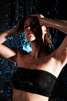 Wet beautiful woman under the falling drops of rain - photo in studio with blue light