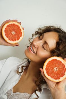 Portrait of pretty middle-aged woman with curly hair with grapefruit at home - light room. Happiness, beauty and health - vertical photo