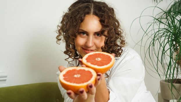 Portrait of pretty middle-aged woman with curly hair with grapefruit at home - light room. The concept of happiness, beauty and health