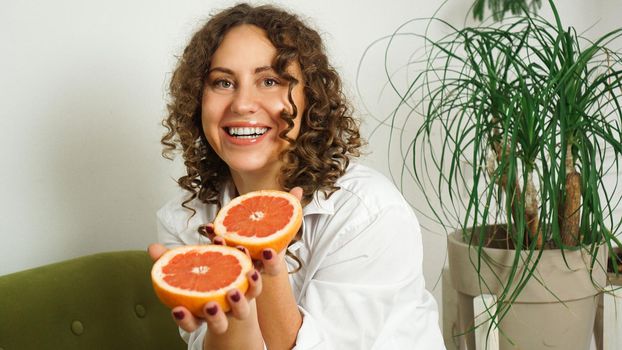 Portrait of pretty middle-aged woman with curly hair with grapefruit at home - light room. The concept of happiness, beauty and health