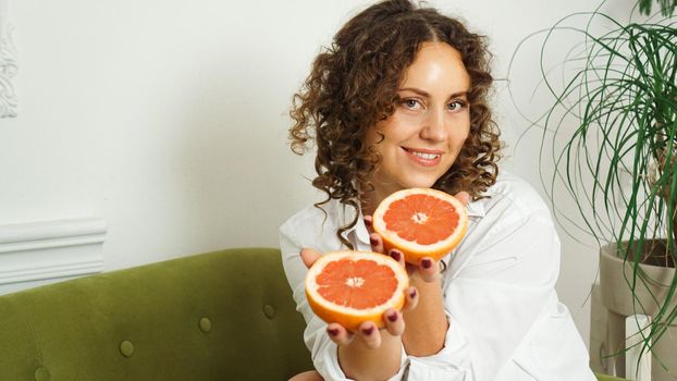 Portrait of pretty middle-aged woman with curly hair with grapefruit at home - light room. The concept of happiness, beauty and health