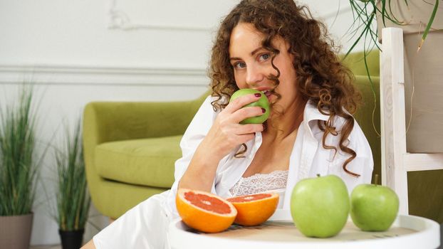 Young woman eating green apple at home. Healthy nutrition, diet food concept. Close-up portrait of beautiful young woman eating organic green apple.