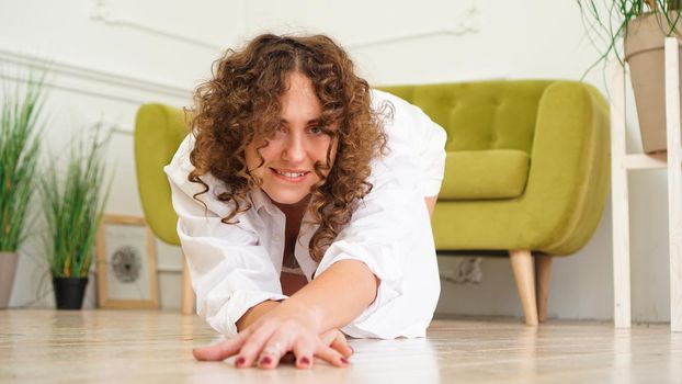 Sexy woman in white shirt on wooden floor - Portrait of pretty middle-aged woman with curly hair at home - light room.