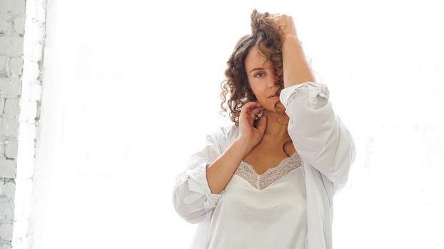 Sexy young woman in white shirt in bedroom, white light from window on the background