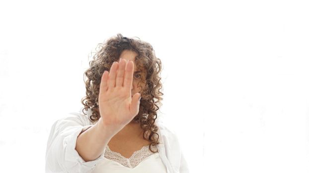 Woman making stop gesture with her hand isolated on a white background. Beautiful woman with curly hair in white lingerie at home