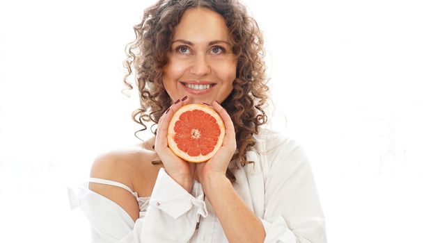 Portrait of pretty middle-aged woman with curly hair with grapefruit at home - white background. The concept of happiness, beauty and health