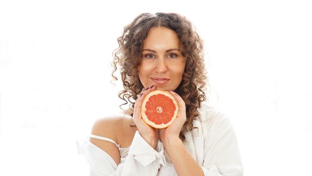 Portrait of pretty middle-aged woman with curly hair with grapefruit at home - white background. The concept of happiness, beauty and health